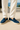 men’s navy suede loafers styled with white linen pants on a sunlit terrace, beige tiled floor and coastal background — smart casual summer shoes for men.